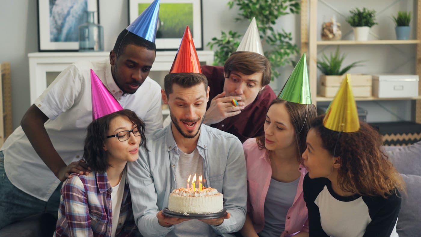 Friends in party hats gathered around a birthday cake with lit candles